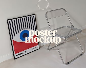 Könnte beinhalten: Ein schwarzer gerahmter Poster mit einer roten, weißen und blauen Augengrafik und dem Text "BAHAUS" und "ANSTRAKTE KUNST" auf weißem Hintergrund. Ein silberner Klappstuhl steht im Vordergrund.