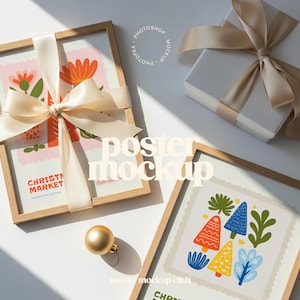 Puede incluir: Dos carteles enmarcados con coloridos diseños florales y de árboles, atados con cintas color crema. También hay una caja de regalo blanca con una cinta a juego y un adorno dorado. Los carteles están etiquetados como "Christmas Market".