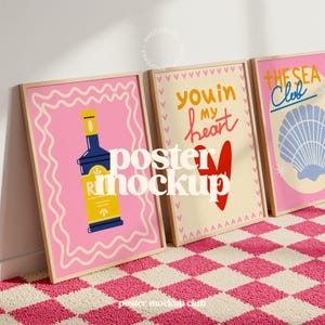 May include: Three framed posters with vibrant illustrations. One shows a bottle design on a pink background, another says "you in my heart", and the last one says "The Sea Club" with a seashell. The posters are on a pink and white checkered rug.