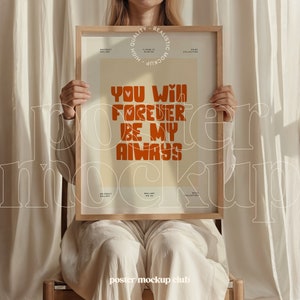 May include: A person holding a framed poster with the text "You will forever be my always" in orange letters on a cream background. The poster is in a wooden frame.
