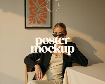 May include: A woman wearing a black blazer and a beige dress sits at a table with a glass of wine in her hand. A framed poster with an abstract orange and blue design hangs on the wall behind her. The poster has the text "PAPIERS DECOUPES" at the top and "ART EXHIBITION" at the bottom. The text "poster mockup" is superimposed on the image.