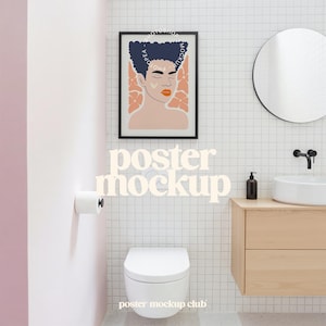May include: A black framed poster with a colorful illustration of a person with closed eyes and pink flowers. The poster is hanging in a bathroom with white tile, a toilet, and a sink.