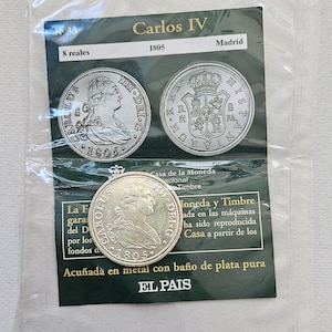 Op de afbeelding: Een verzameling van drie zilveren munten uit 1805, met een portret van Carlos IV. De munten worden getoond in een transparante plastic hoes met de tekst "Carlos IV" en "8 reales".