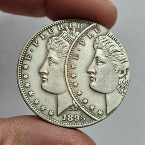Puede incluir: Una moneda de plata con dos perfiles enfrentados. La moneda tiene el texto "E PLURIBUS UNUM" y "LIBERTY" alrededor de los bordes, con el año "1893" en la parte inferior. La moneda está sujeta entre dos dedos.