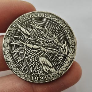 Puede incluir: Una moneda de color plateado con una imagen detallada de la cabeza de un dragón y el texto "EXPLURIBUS UNUM" y "1921".