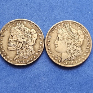 Puede incluir: Dos monedas de plata Morgan, una con un diseño de calavera y otra con el perfil de una mujer. Ambas monedas están fechadas en 1878 y tienen las inscripciones "E PLURIBUS UNUM" y "LIBERTY". Las monedas están sobre un fondo azul.
