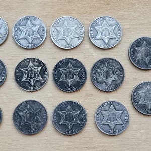 May include: A collection of 15 silver-colored US half dollar coins with a star design. The coins are dated from 1863 to 1887.