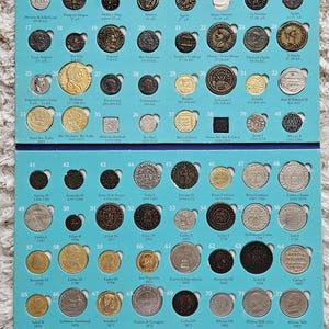 Puede incluir: Colección de monedas antiguas expuestas sobre un fondo azul. Las monedas, de varios tamaños y diseños, presentan inscripciones y retratos. La disposición está organizada en filas y columnas, mostrando moneda histórica.
