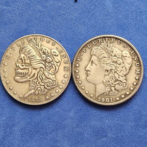 Puede incluir: Dos monedas de plata sobre una superficie azul. Una moneda presenta un diseño de calavera con el año 1878, y la otra muestra el perfil de una mujer con el año 1901. Ambas monedas tienen detalles intrincados y texto en los bordes.