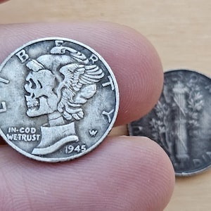 Puede incluir: Primer plano de dos monedas de diez centavos de plata Mercury. La moneda delantera, fechada en 1945, muestra el perfil de una mujer con un gorro alado y la inscripción "IN GOD WE TRUST". La segunda moneda es parcialmente visible.
