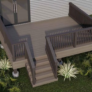 May include: A composite deck with stairs and railings, attached to a house. The deck is brown, with matching railings and stairs. The deck is surrounded by green grass and plants. The house has a gray exterior and a glass door.