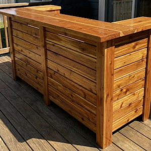 Peut inclure: Un bar extérieur en bois avec une finition naturelle. Le bar est construit à partir de planches horizontales et comporte un comptoir et une section inférieure. Le bar est conçu pour une utilisation en extérieur et est en bois.