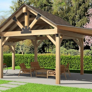 Puede incluir: Un cenador de madera para exteriores con techo a dos aguas, sostenido por postes robustos. La estructura cuenta con una zona de estar con sillas y una mesa. Dos bicicletas están aparcadas cerca. El cenador está situado en un patio de hormigón con césped verde y árboles al fondo.