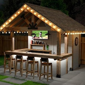 Può includere: Bar all'aperto in legno con tetto a scandole marrone, luci a corda e TV integrata. Il bar ha un bancone con sgabelli e una mensola in legno che espone bottiglie. Il bar è in un giardino.