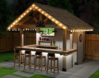 May include: Wooden outdoor bar with a brown shingled roof, fairy lights, and a built-in TV. The bar has a countertop with bar stools and a wooden shelf displaying bottles. The bar is in a garden setting.