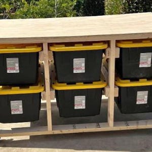May include: A wooden storage unit with six black bins with yellow lids. The unit is constructed from light-colored wood and has a flat top. The bins are arranged in two rows of three and sit on wheels.