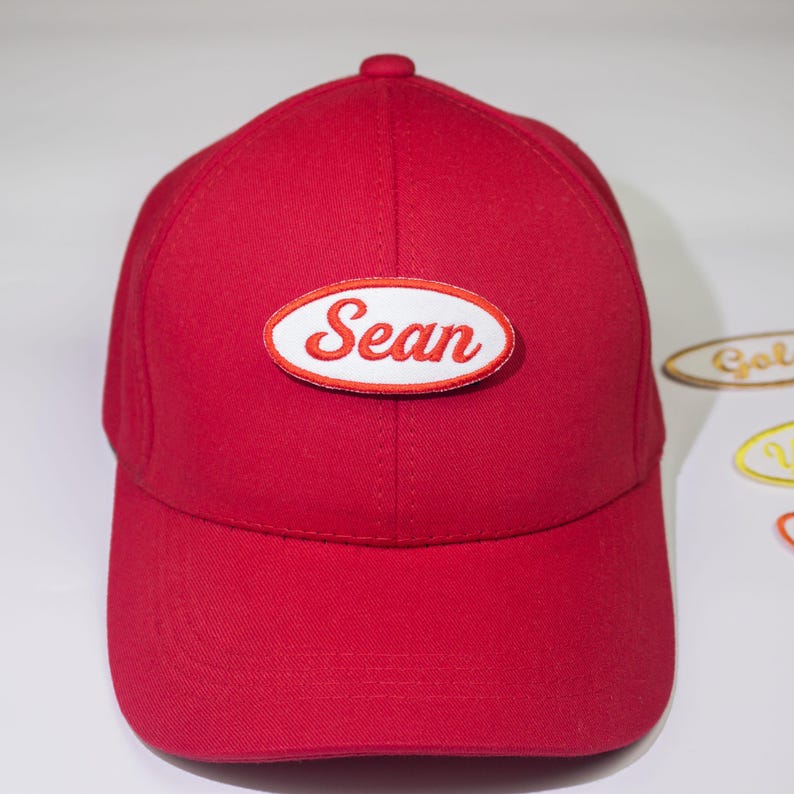 May include: Red baseball cap with a white oval patch that says "Sean" in red embroidered letters.