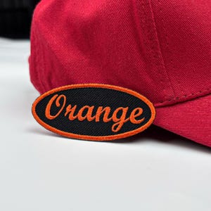 May include: A red baseball cap with a black oval patch that says "Orange" in orange embroidery.