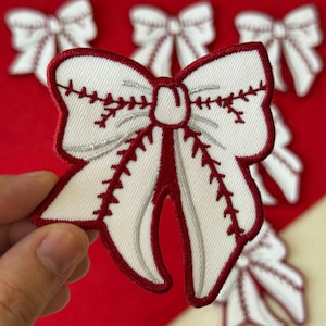 May include: White fabric bow patch with red stitching and a red border. The bow has a baseball stitch design with silver accents. Several bow patches are visible against a red background.