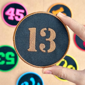 May include: Embroidered patches with numbers in various colours. The main patch is black with the number "13" in gold. Other patches display numbers such as "45" and "53" in pink, green, and yellow. The patches are round with a stitched border.