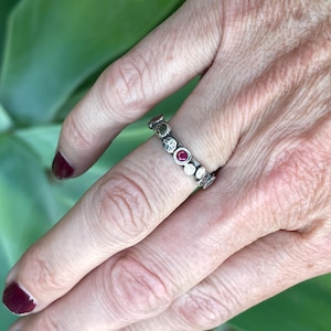 Puede incluir: Un anillo de plata con peque&ntilde;os c&iacute;rculos texturizados engastados con piedras preciosas rojas.