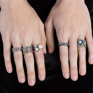 Puede incluir: Un maniqu&iacute; de mano lleva una pila de anillos de plata con piedras preciosas de colores. Los anillos est&aacute;n apilados en dos dedos de la mano izquierda. Los anillos son de plata y tienen una variedad de piedras preciosas, incluyendo turquesa, rosa y rojo.