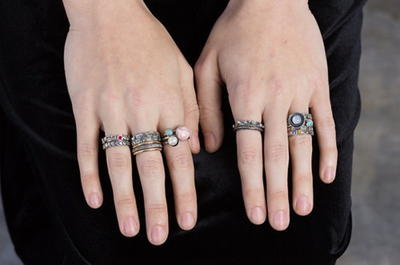 Puede incluir: Un maniqu&iacute; de mano lleva una pila de anillos de plata con piedras preciosas de colores. Los anillos est&aacute;n apilados en dos dedos de la mano izquierda. Los anillos son de plata y tienen una variedad de piedras preciosas, incluyendo turquesa, rosa y rojo.