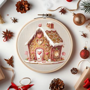 Könnte beinhalten: Ein Stickrahmen mit einem Lebkuchenhaus-Design. Das Haus ist mit Herzen, Süßigkeiten und Schnee verziert und auf einem neutralen Stoff angebracht. Weihnachtsschmuck und festliche Dekorationen umgeben den Rahmen.