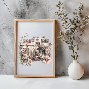 Puede incluir: Una impresión enmarcada de una cámara vintage con delicadas flores rosas y blancas que la rodean. La cámara es plateada y dorada con una lente negra. El fondo es azul claro.