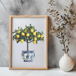 May include: A framed cross-stitch artwork depicting a lemon tree in a blue and white ceramic pot. The tree has green leaves and yellow lemons.