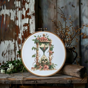 Puede incluir: Un aro de bordado de punto de cruz con un diseño de reloj de arena vintage. El reloj de arena es de vidrio y tiene una calavera en la parte inferior. El reloj de arena está rodeado de enredaderas y rosas.
