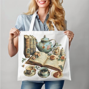 Puede incluir: Una bolsa de tela blanca con una tetera azul y blanca, dos tazas de té, un libro y pasteles impresos en ella. La bolsa de tela tiene un diseño floral azul y blanco.