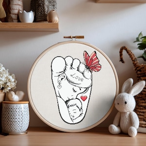 May include: A cross-stitch embroidery hoop featuring a black and white design of a mother and child. A red butterfly rests on the mother's head, and the word "Love" is written on the design. A red heart is also included.