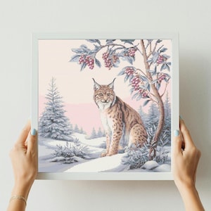 May include: A framed cross-stitch featuring a lynx in a winter forest. The lynx has brown and tan fur, set against a pink and white backdrop. The artwork includes a tree with pink berries and snow-covered fir trees.