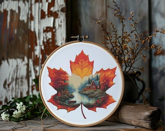May include: A cross-stitch embroidery in a wooden hoop, featuring a maple leaf design. The leaf is in shades of orange and red, with a detailed landscape scene of a cabin by a lake. The background is a rustic wooden surface.