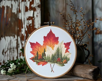 May include: A cross-stitch embroidery hoop featuring a vibrant autumn leaf design. The leaf showcases a gradient of red, orange, and yellow hues, with a detailed forest scene in the center. The embroidery is set in a wooden hoop.