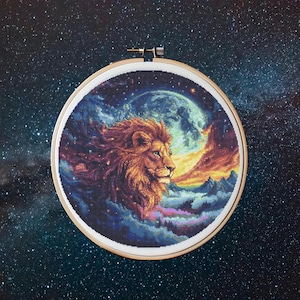 May include: A cross-stitch embroidery depicting a lion's head in profile, set within a wooden hoop. The artwork features a golden-maned lion against a backdrop of a full moon, mountains, and a starry night sky.