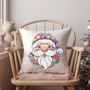 Peut inclure: Un coussin carré blanc avec un motif de visage de Père Noël coloré. Le Père Noël a une barbe blanche et un chapeau patchwork de différentes couleurs. Le coussin est posé sur une chaise en bois, avec un sapin de Noël en arrière-plan.