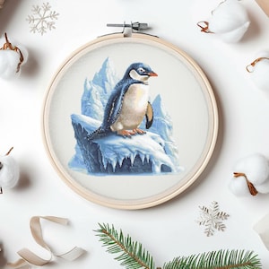 May include: A cross-stitch pattern of a penguin standing on a snowy, icy cliff. The penguin is black and white with a yellow beak. The background is a light blue.
