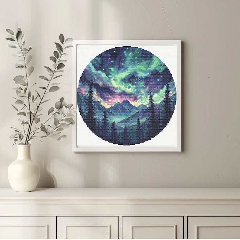 Puede incluir: Una impresi&oacute;n circular enmarcada de una cordillera con una aurora boreal vibrante en el cielo. Las monta&ntilde;as est&aacute;n silueteados contra el cielo colorido, que est&aacute; lleno de estrellas.