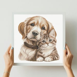 Può includere: Uno schema a punto croce incorniciato raffigurante un cucciolo color oro con un collare marrone scuro seduto accanto a un piccolo gattino tigrato marrone. L'opera mostra punti dettagliati dei due animali su uno sfondo bianco in una cornice bianca.
