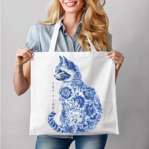 May include: White tote bag featuring a blue and white floral design of a cat. The text "TEA TIME" is printed vertically on the left side of the bag.