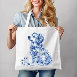 May include: White tote bag with a blue and white floral dog design. The dog is sitting, its body made of blue floral patterns. The tote bag has two white handles. The design is reminiscent of Delftware.