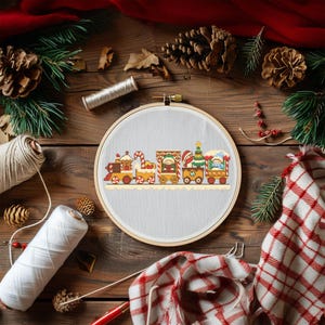 Puede incluir: Un bastidor de bordado con un diseño de tren navideño. Los vagones del tren están decorados con bastones de caramelo, Papá Noel y un árbol de Navidad. El bordado está sobre una tela neutra, rodeado de elementos de madera y decoración navideña.