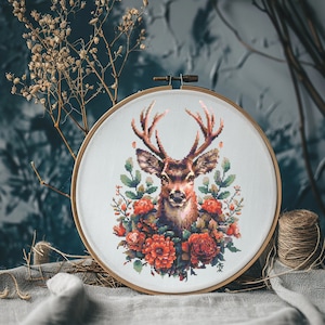 May include: Cross-stitch embroidery hoop featuring a detailed image of a deer's head with antlers, surrounded by red and green floral accents.