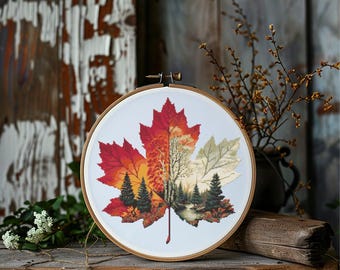 May include: A cross-stitch embroidery of a maple leaf in a wooden hoop. The leaf is divided into sections of red, orange, and green, with a forest scene stitched into the center. The embroidery is displayed on a rustic wooden surface.
