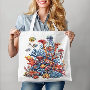 May include: A white tote bag with a colorful design of coral reefs, fish, and jellyfish. The design is vibrant and detailed, featuring a variety of marine life.