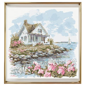 May include: A white cottage with a brown roof sits on a rocky shore with pink flowers in the foreground. The cottage has a porch with a white picket fence. The sea is in the background with a sailboat in the distance. The sky is blue with white clouds.