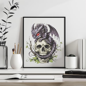 May include: Framed artwork featuring a detailed illustration of a dark purple dragon with red eyes perched atop a human skull. The skull is surrounded by green leaves and vines, set against a white background.