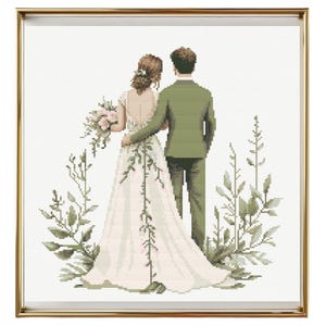 May include: A bride and groom stand back to back, facing away from the viewer. The bride is wearing a white wedding dress with a long train. The groom is wearing a green suit. They are surrounded by green foliage.